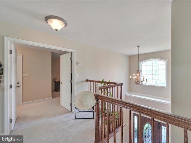 hallway featuring baseboards, light carpet, a notable chandelier, and an upstairs landing
