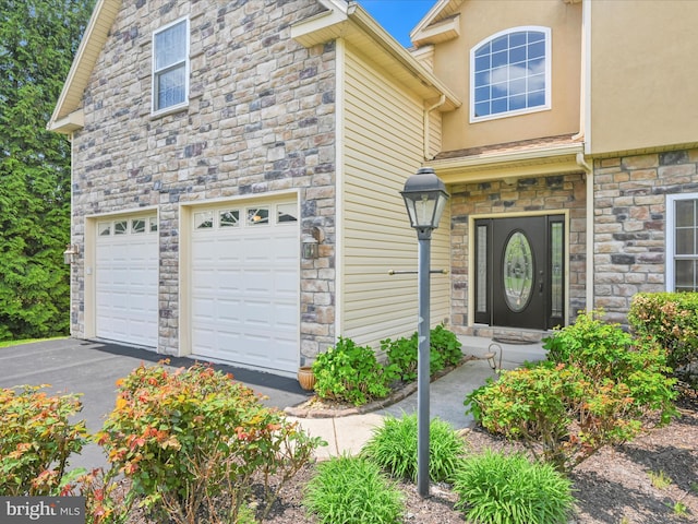 view of front of property with an attached garage, driveway, stone siding, and stucco siding