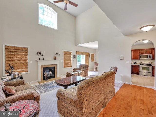 living area featuring a high end fireplace, ceiling fan, a high ceiling, and arched walkways