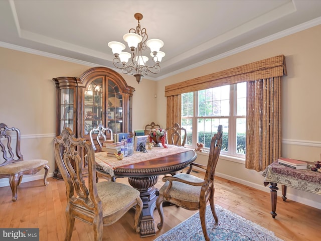 dining area featuring crown molding, a raised ceiling, baseboards, a notable chandelier, and light wood-style floors