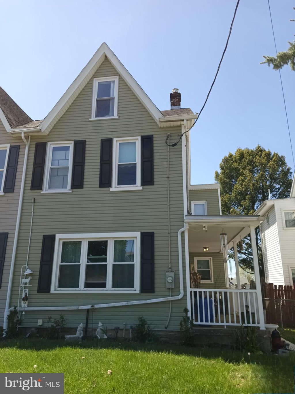 view of front of property with a porch, a front yard, fence, and a chimney