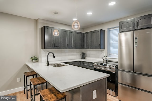 kitchen featuring a sink, a kitchen bar, tasteful backsplash, a peninsula, and appliances with stainless steel finishes