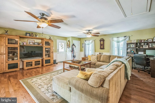 living area with a wainscoted wall, a ceiling fan, attic access, and wood finished floors