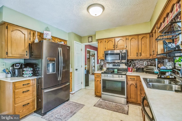 kitchen with a sink, light countertops, a textured ceiling, brown cabinetry, and stainless steel appliances