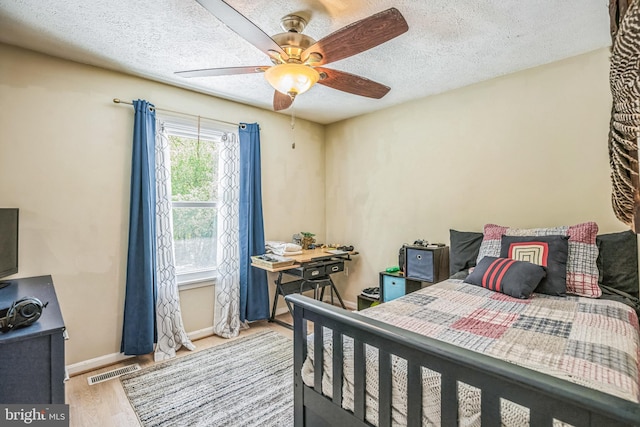 bedroom with ceiling fan, a textured ceiling, visible vents, wood finished floors, and baseboards