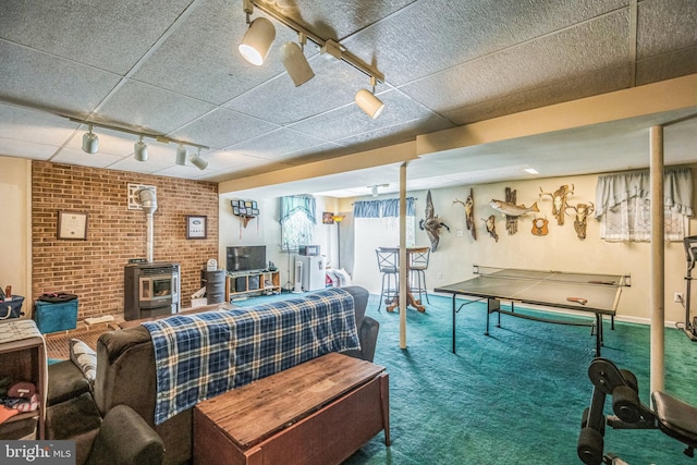 recreation room with brick wall, a paneled ceiling, a wood stove, rail lighting, and carpet