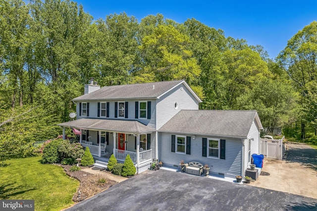 colonial home featuring a porch, a chimney, a front yard, aphalt driveway, and a shingled roof