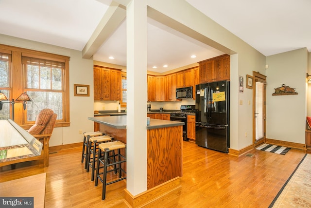 kitchen featuring a breakfast bar area, recessed lighting, black appliances, and light wood-style floors