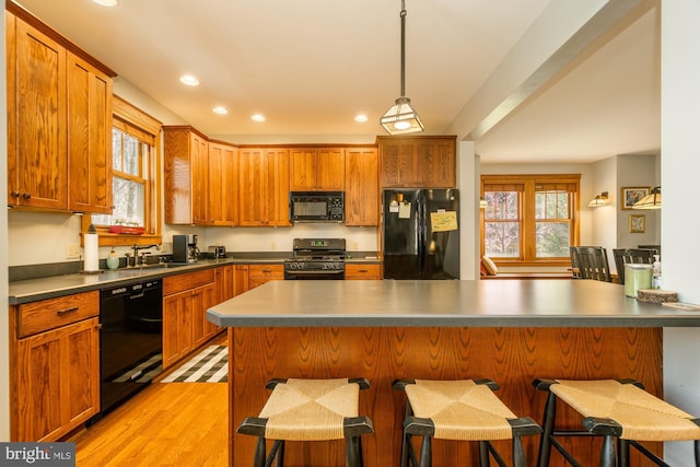 kitchen featuring a breakfast bar area, decorative light fixtures, a sink, black appliances, and recessed lighting