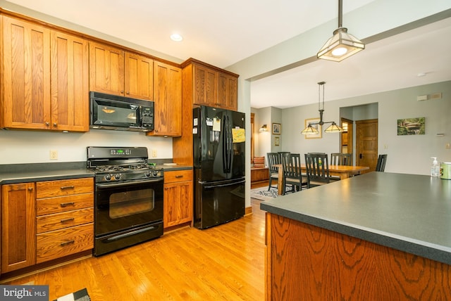 kitchen with brown cabinetry, pendant lighting, dark countertops, light wood finished floors, and black appliances