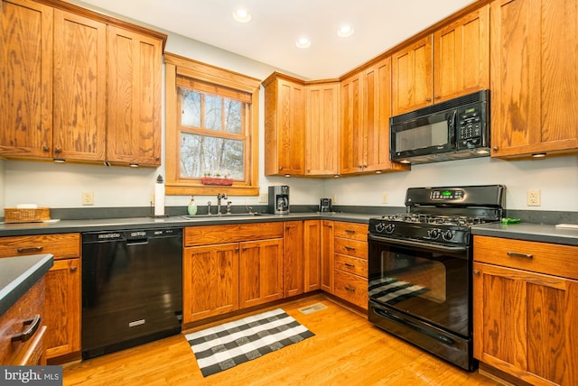 kitchen with dark countertops, a sink, black appliances, light wood finished floors, and recessed lighting