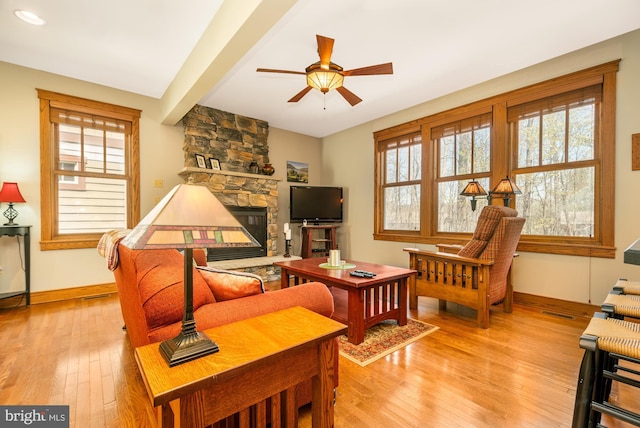 living area with baseboards, a ceiling fan, light wood finished floors, and a fireplace