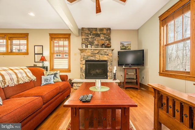 living room with a stone fireplace, a ceiling fan, light wood-style flooring, and a healthy amount of sunlight