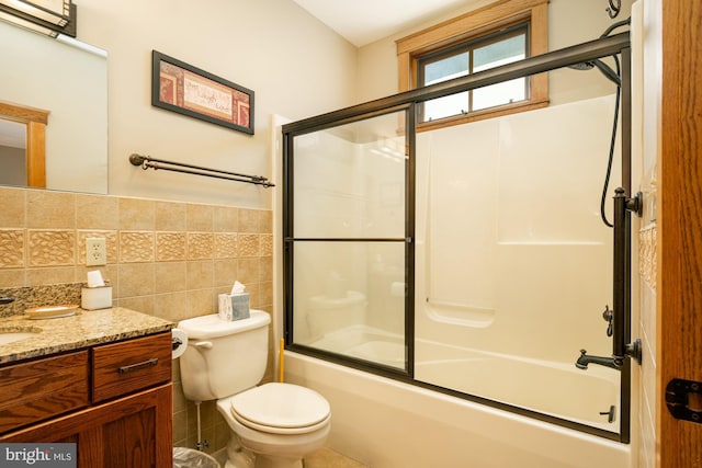 bathroom featuring vanity, combined bath / shower with glass door, toilet, and tile walls