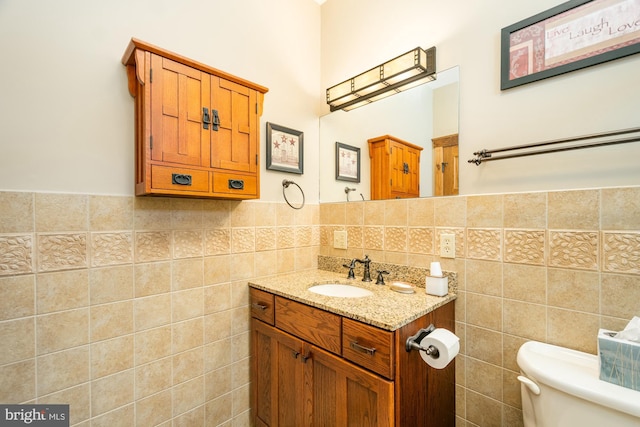 bathroom with tile walls, a wainscoted wall, vanity, and toilet