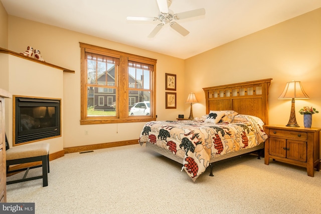 bedroom with carpet floors, visible vents, a glass covered fireplace, baseboards, and a ceiling fan