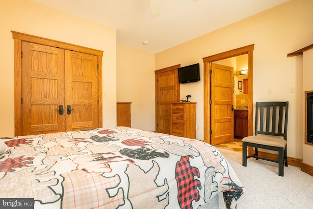 bedroom featuring ceiling fan, light colored carpet, baseboards, a closet, and ensuite bath