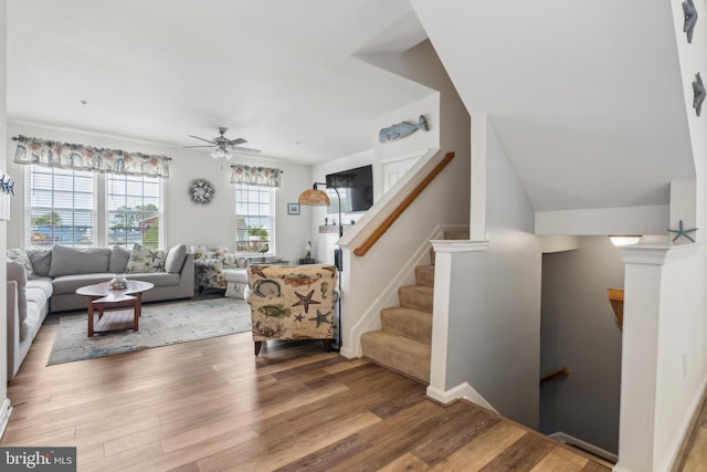 living room featuring a ceiling fan, wood finished floors, and stairway