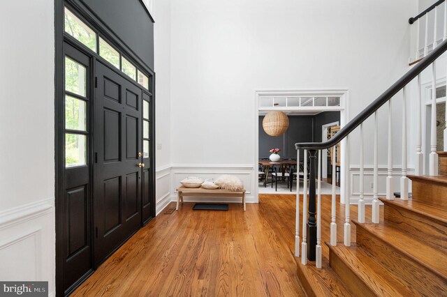foyer entrance with stairs, a towering ceiling, a decorative wall, wood finished floors, and wainscoting