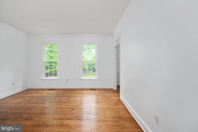 spare room with crown molding, baseboards, and light wood-style floors