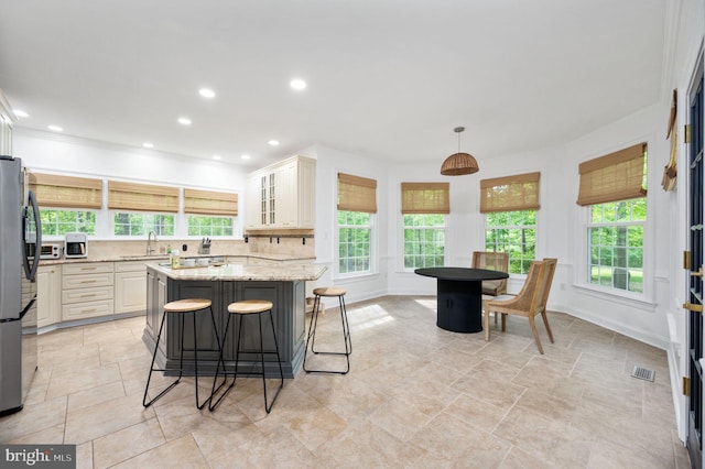 kitchen featuring a kitchen breakfast bar, decorative backsplash, visible vents, a sink, and light stone counters