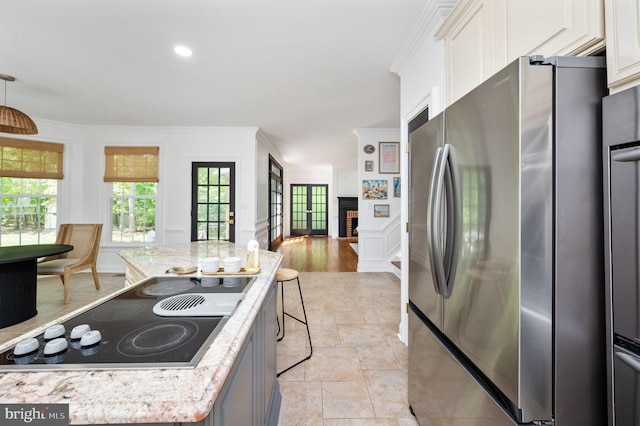 kitchen with freestanding refrigerator, ornamental molding, stone finish floor, black electric cooktop, and white cabinets