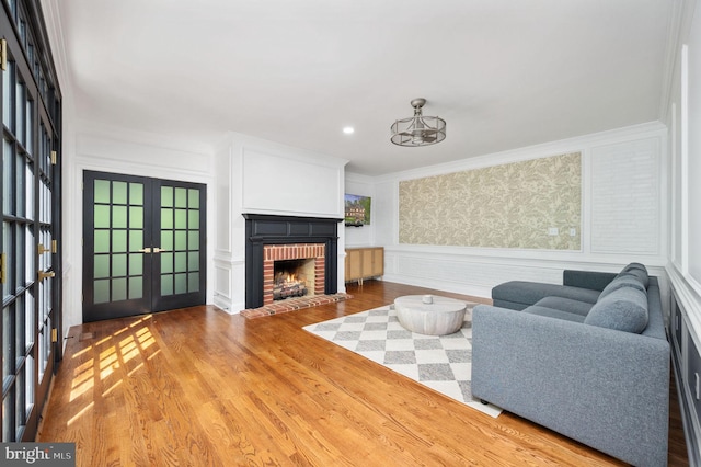 living area featuring ornamental molding, wainscoting, wood finished floors, a fireplace, and french doors