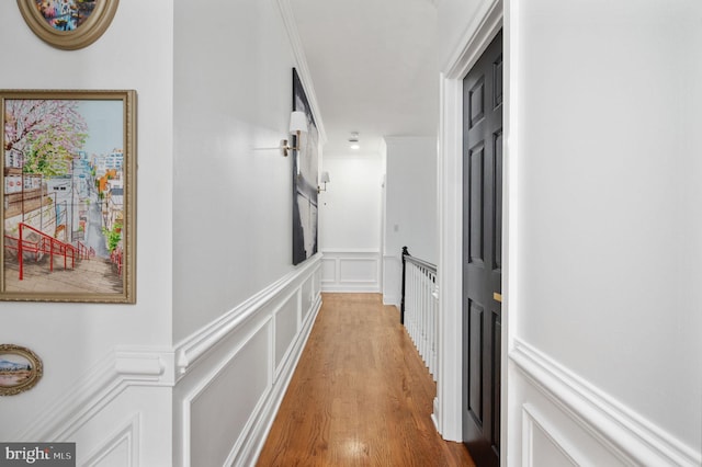 hall featuring wainscoting, a decorative wall, and wood finished floors