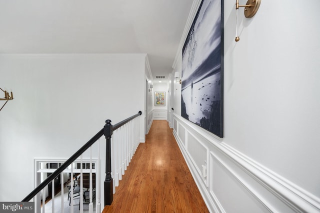corridor featuring crown molding, visible vents, wainscoting, wood finished floors, and an upstairs landing