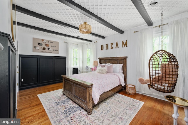 bedroom featuring beamed ceiling, multiple windows, and light wood-style floors