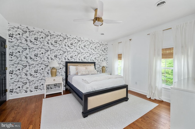 bedroom featuring ceiling fan, baseboards, wallpapered walls, wood finished floors, and visible vents