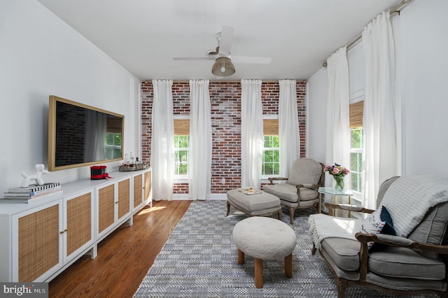 living area featuring ceiling fan, wood finished floors, and brick wall