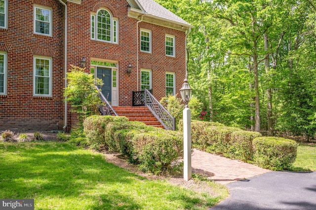 colonial inspired home featuring brick siding, a shingled roof, and a front yard