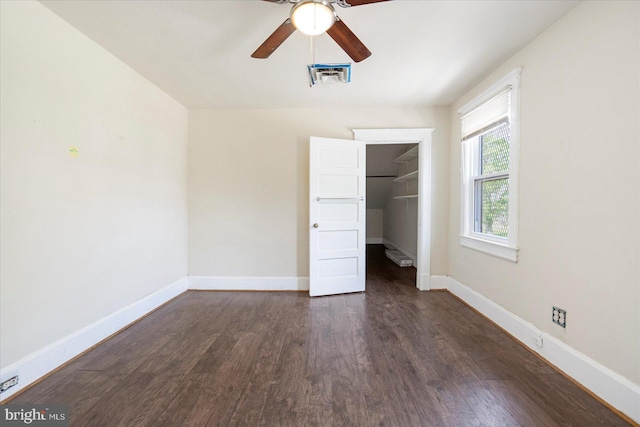 unfurnished bedroom with dark wood-style flooring, a walk in closet, baseboards, visible vents, and a closet