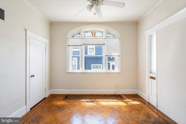 empty room with crown molding, baseboards, ceiling fan, and visible vents