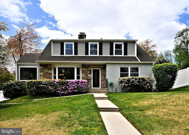 view of front of house with a chimney, a shingled roof, a front lawn, and stone siding
