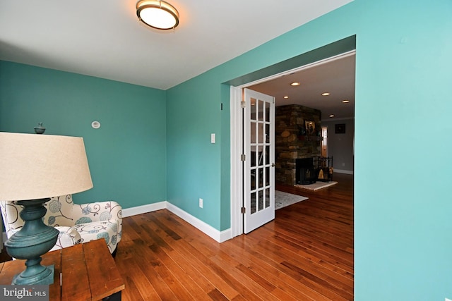 sitting room with wood finished floors, a stone fireplace, and baseboards
