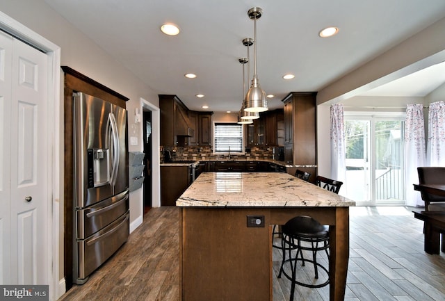 kitchen featuring a breakfast bar area, stainless steel appliances, dark wood-style floors, a center island, and dark brown cabinetry