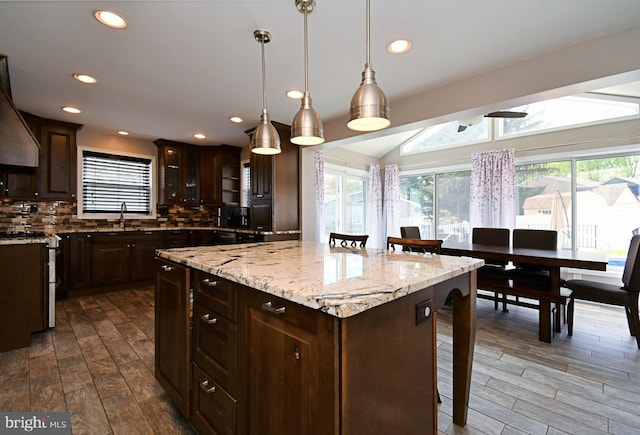 kitchen featuring decorative backsplash, a sink, dark brown cabinetry, a center island, and a kitchen bar