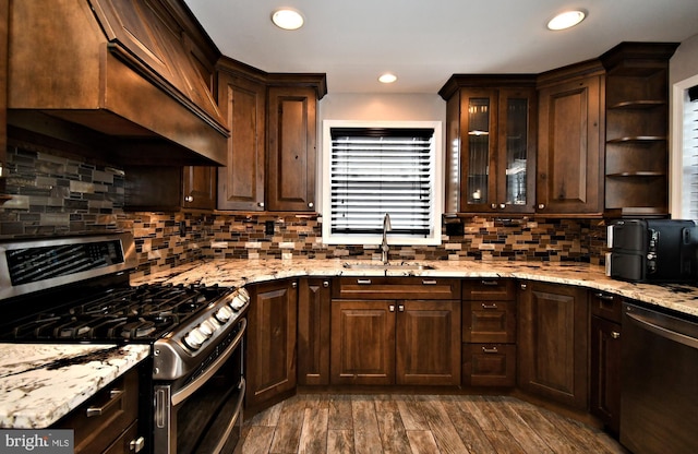 kitchen with dark wood finished floors, custom range hood, appliances with stainless steel finishes, dark brown cabinets, and a sink