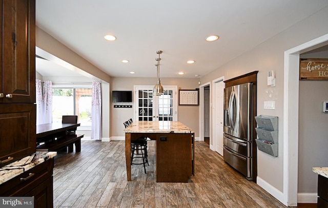 kitchen featuring dark wood finished floors, dark brown cabinetry, stainless steel fridge, a kitchen island, and a kitchen breakfast bar