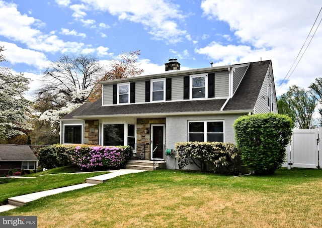 view of front of property featuring fence, roof with shingles, a front yard, and stone siding