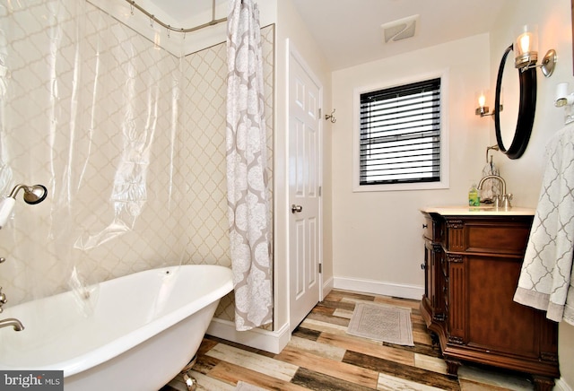 full bathroom with vanity, a soaking tub, wood finished floors, and baseboards
