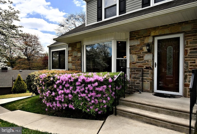 property entrance with stone siding and a shingled roof