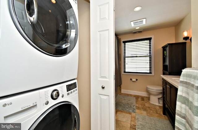 laundry area with laundry area, stacked washer / dryer, stone finish floor, baseboards, and visible vents