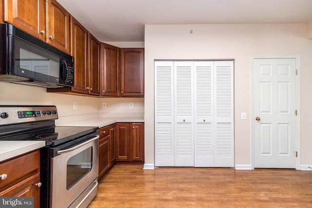 kitchen featuring light countertops, stainless steel electric stove, black microwave, and light wood-style flooring