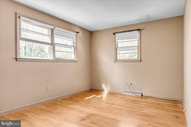 spare room featuring baseboards, wood finished floors, and a wealth of natural light