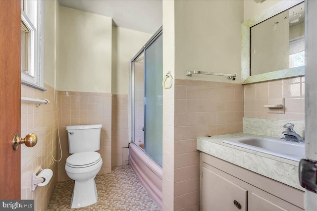 full bath featuring tile walls, enclosed tub / shower combo, a wainscoted wall, toilet, and vanity