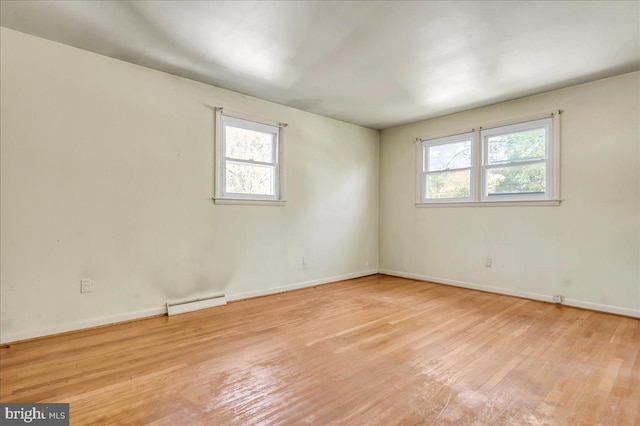 spare room with light wood finished floors, baseboard heating, a wealth of natural light, and baseboards