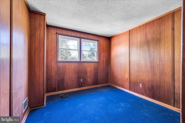 carpeted empty room with baseboards, visible vents, wooden walls, and a textured ceiling